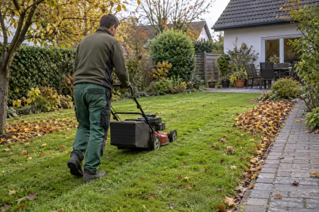 Mitarbeiter mäht einen Rasen beim letzten Schnitt im Herbst